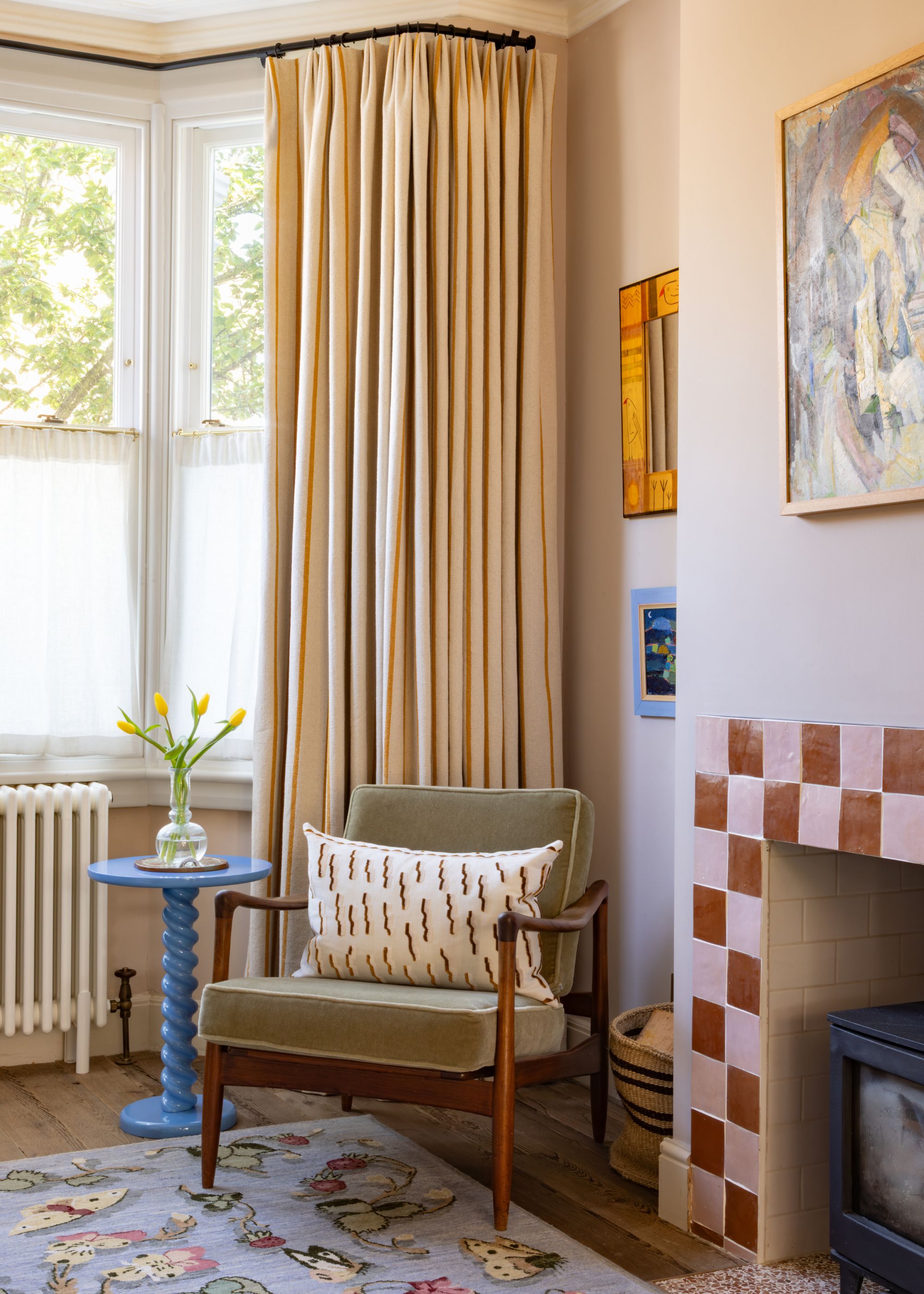 Modern living room with neutral tailored pleated curtains, pink and red fireplace surround, green armchair with blue side table.