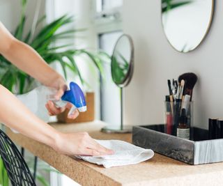 A lasy using a cloth and spray to wipe down a make up desk