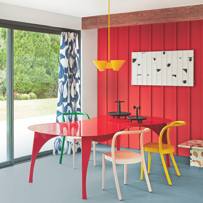 Cherry red pannelled wall with a curved red dining table and multi-coloured chairs