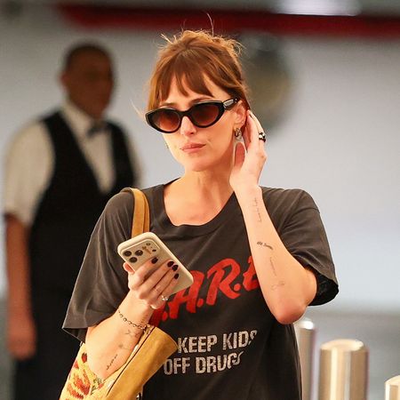 Dakota Johnson wearing a vintage D.A.R.E. T-shirt with silky black puddle pants and high-vamp ballet flats, carrying a Valentino suede tote