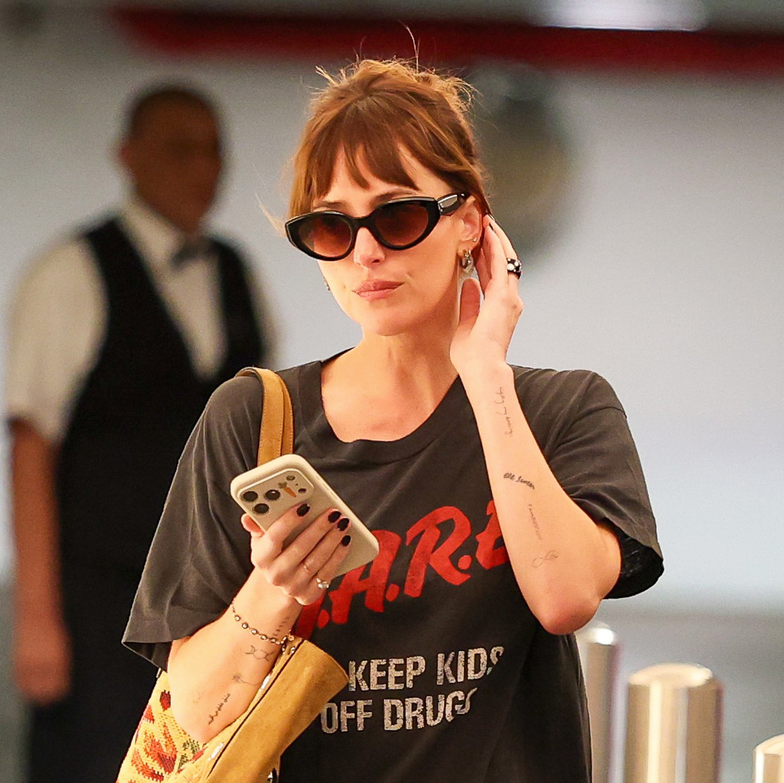 Dakota Johnson wearing a vintage D.A.R.E. T-shirt with silky black puddle pants and high-vamp ballet flats, carrying a Valentino suede tote