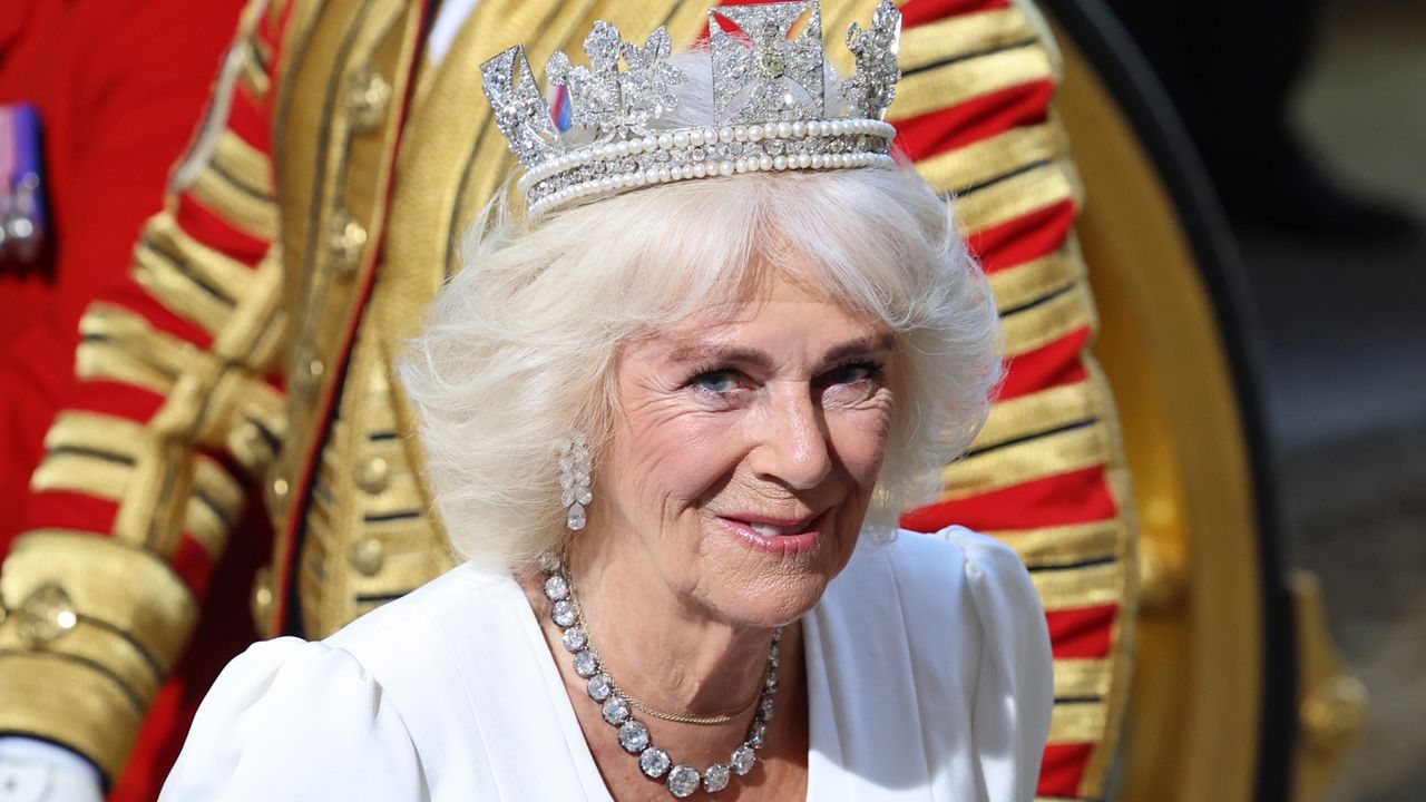 Queen Camilla wears a white dress, a diamond necklace, and a glittering diamond tiara