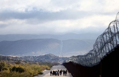 Asylum seeking migrants walk toward a makeshift camp to await processing by the U.S. Border Patrol after crossing into the United States past a gap in the border barrier December 1, 2023 in Jacumba Hot Springs, California.