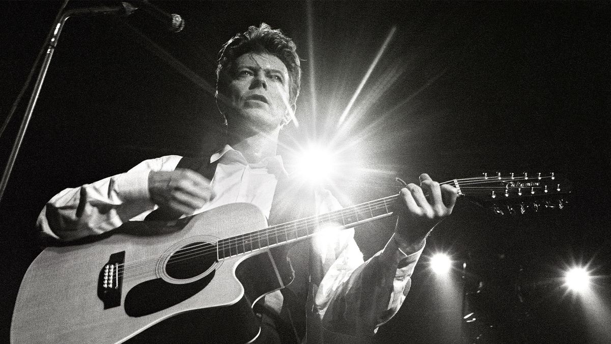 A black and white photo of David Bowie performing on stage with guitar