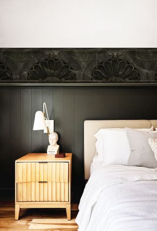 A bedroom with dark panelled walls and an art deco style wallpaper border running along it