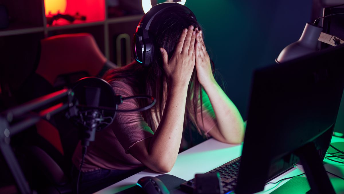 A young woman sitting with her head in her hands in front of a gaming PC.