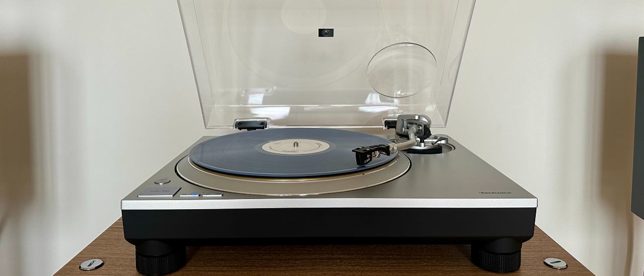 Technics SL-1300G turntable, with the dust cover open, on a wooden platform.