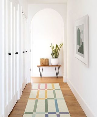 A white entryway with a wooden floor with a colorful runner rug on it