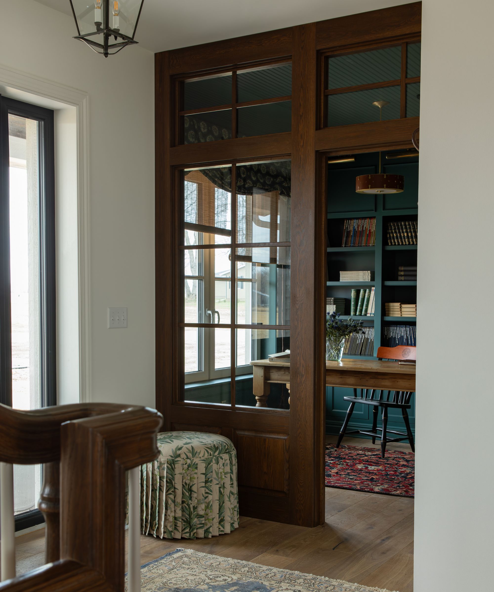 neutral hallway with glass wooden wall divider looking into a cozy small home office color drenched in farrow and ball's inchyra blue
