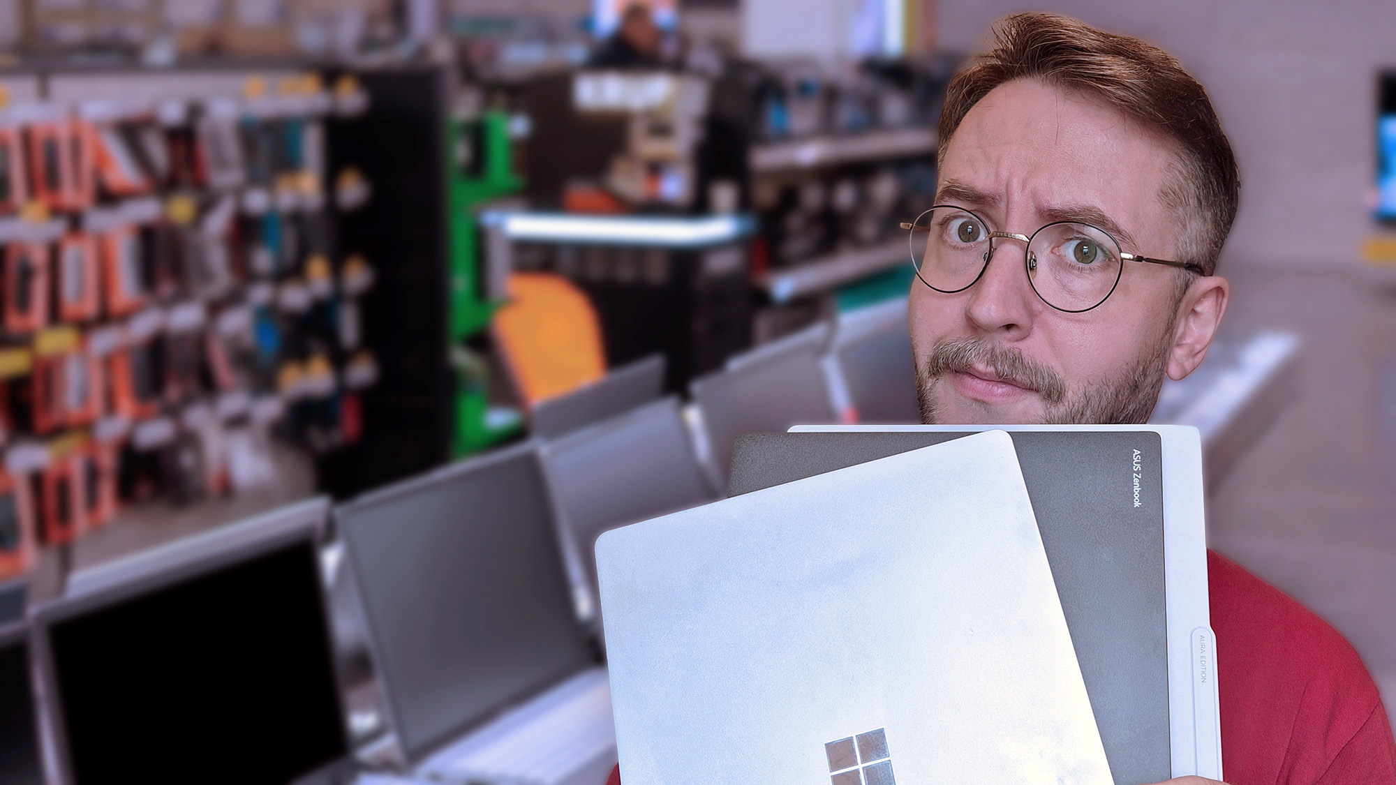 Windows Central Senior Editor Ben Wilson holding two laptops in an electronics store, looking puzzled.