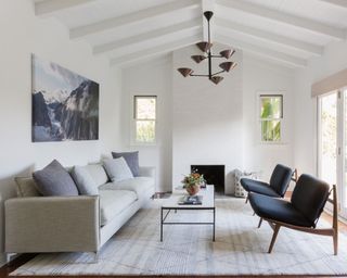Minimalist living room, white walls, vaulted ceiling, gray sofa, dark wood and dark gray armchairs, fireplace, large gray rug