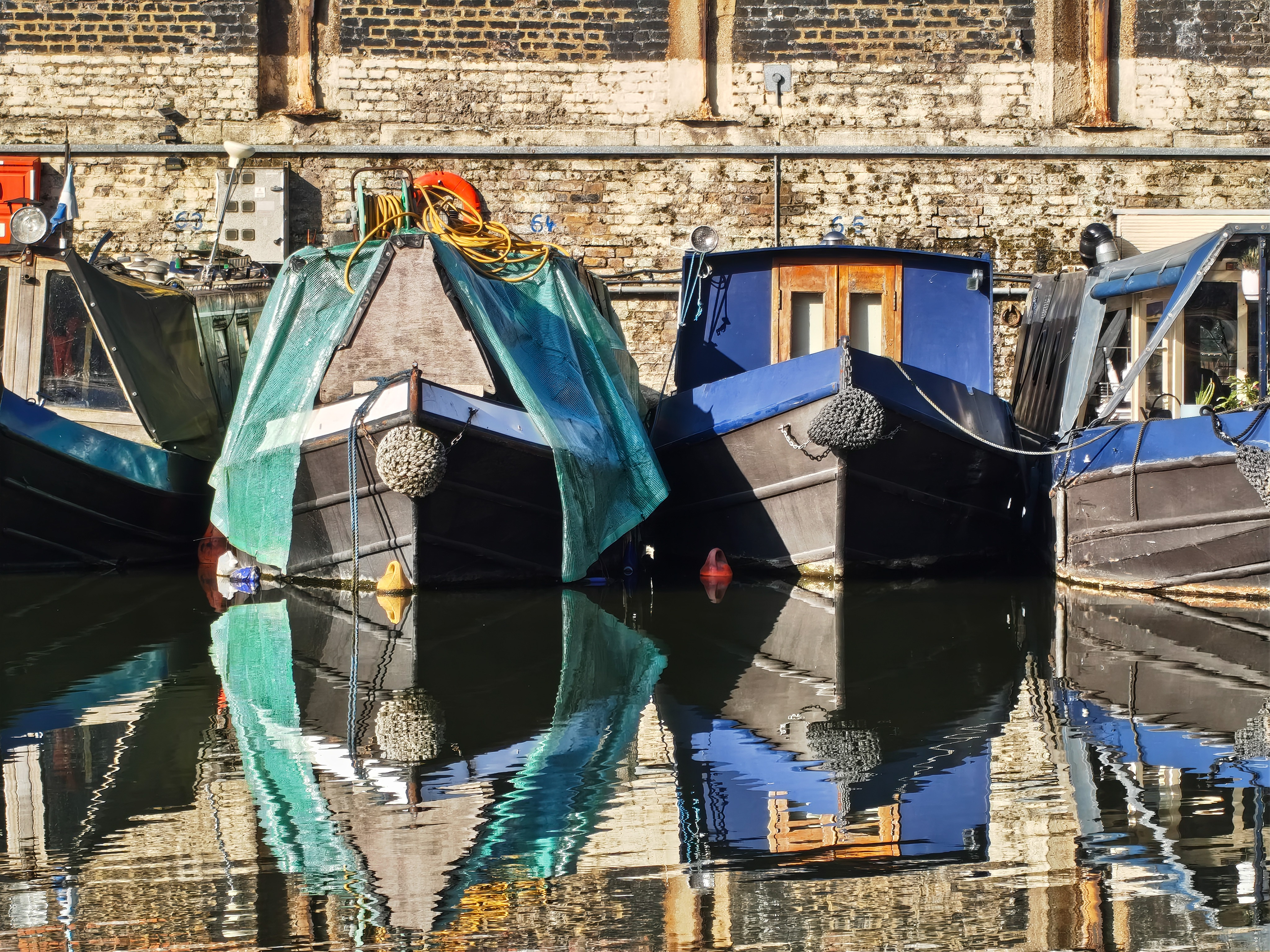 Close-up of canal boats docked along a brick wall with strong reflections in the water, photographed with the Nothing Phone (4a).