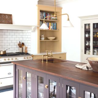 kitchen with white walls and aga, a cream corner cabinet in alcove and dark wooden island with brass and white pendant light