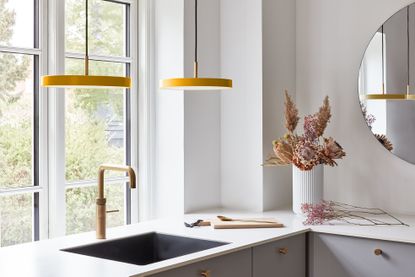 modern yellow pendant lights over a basin with brass tap, white countertop 