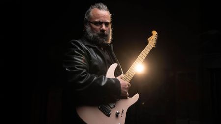 Rick Graham – dressed in black and illuminated with a spotlight, against a black backdrop – holding his pink Charvel signature guitar