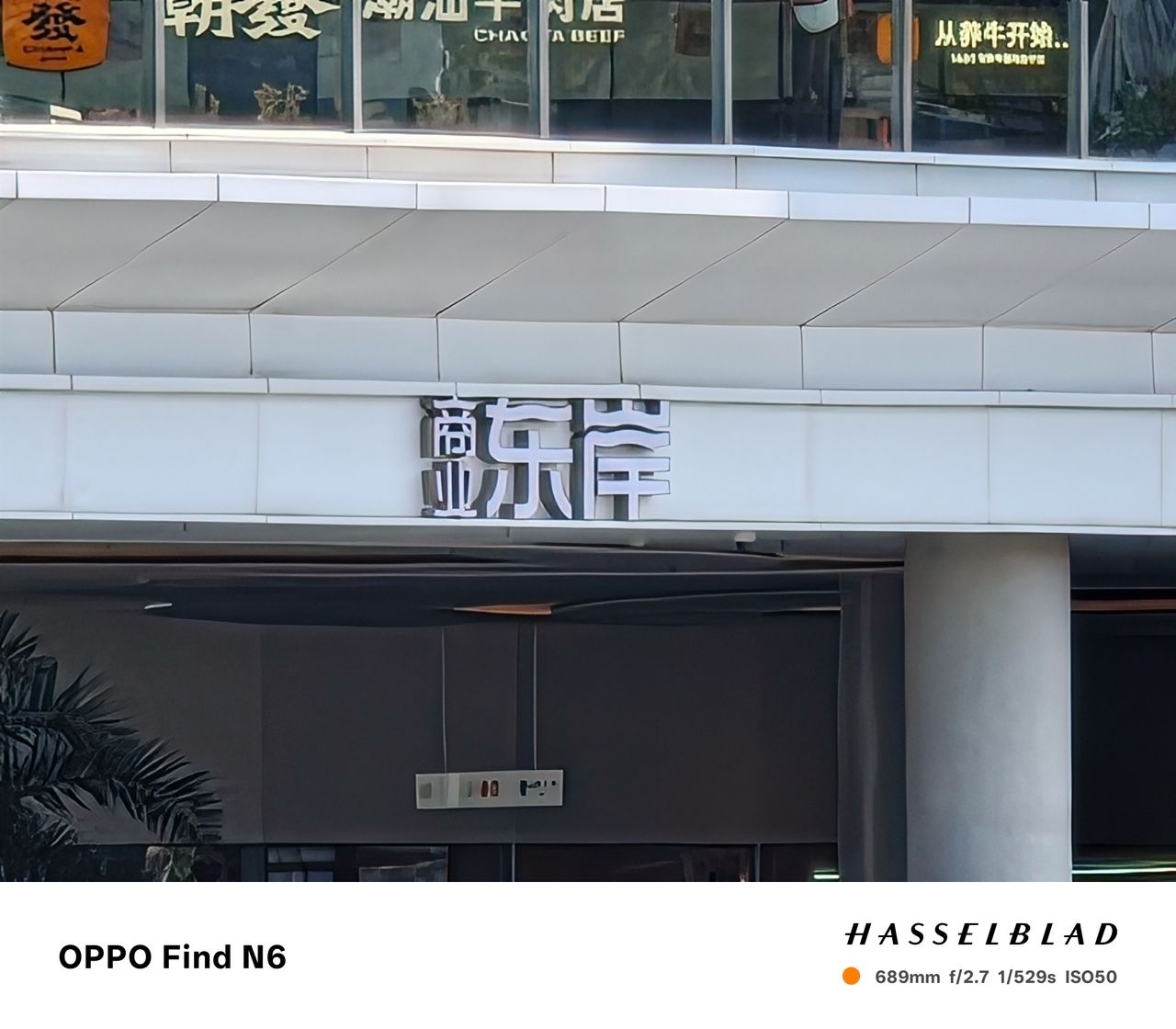 An extreme telephoto close-up focusing on a set of large, silver 3D Chinese characters mounted on a white building beam. Despite the massive zoom, the edges of the characters and the texture of the building materials remain visible.