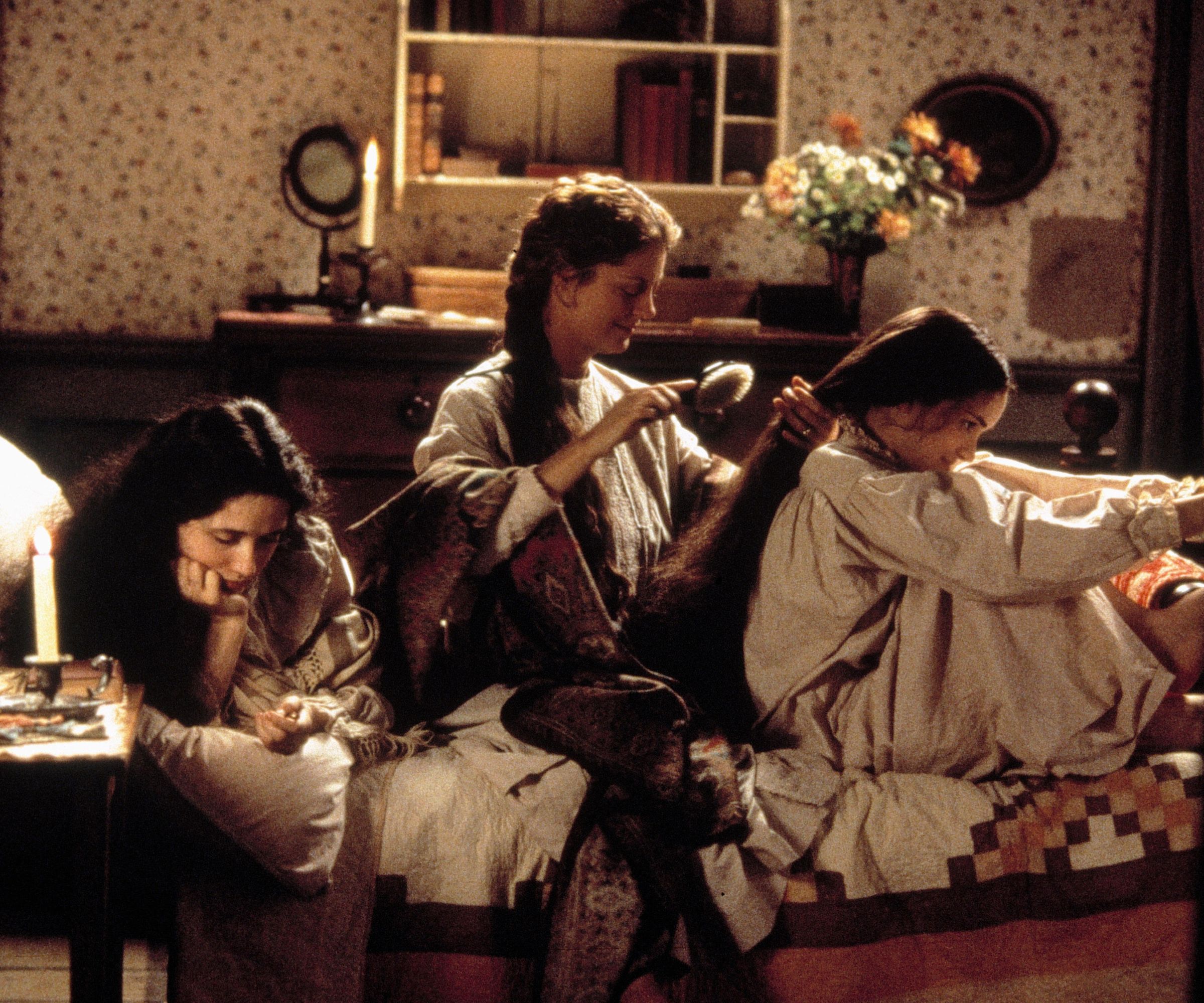 a still from Little Women 1994 with three girls sat on the bed with floral wallpaper and a quilt