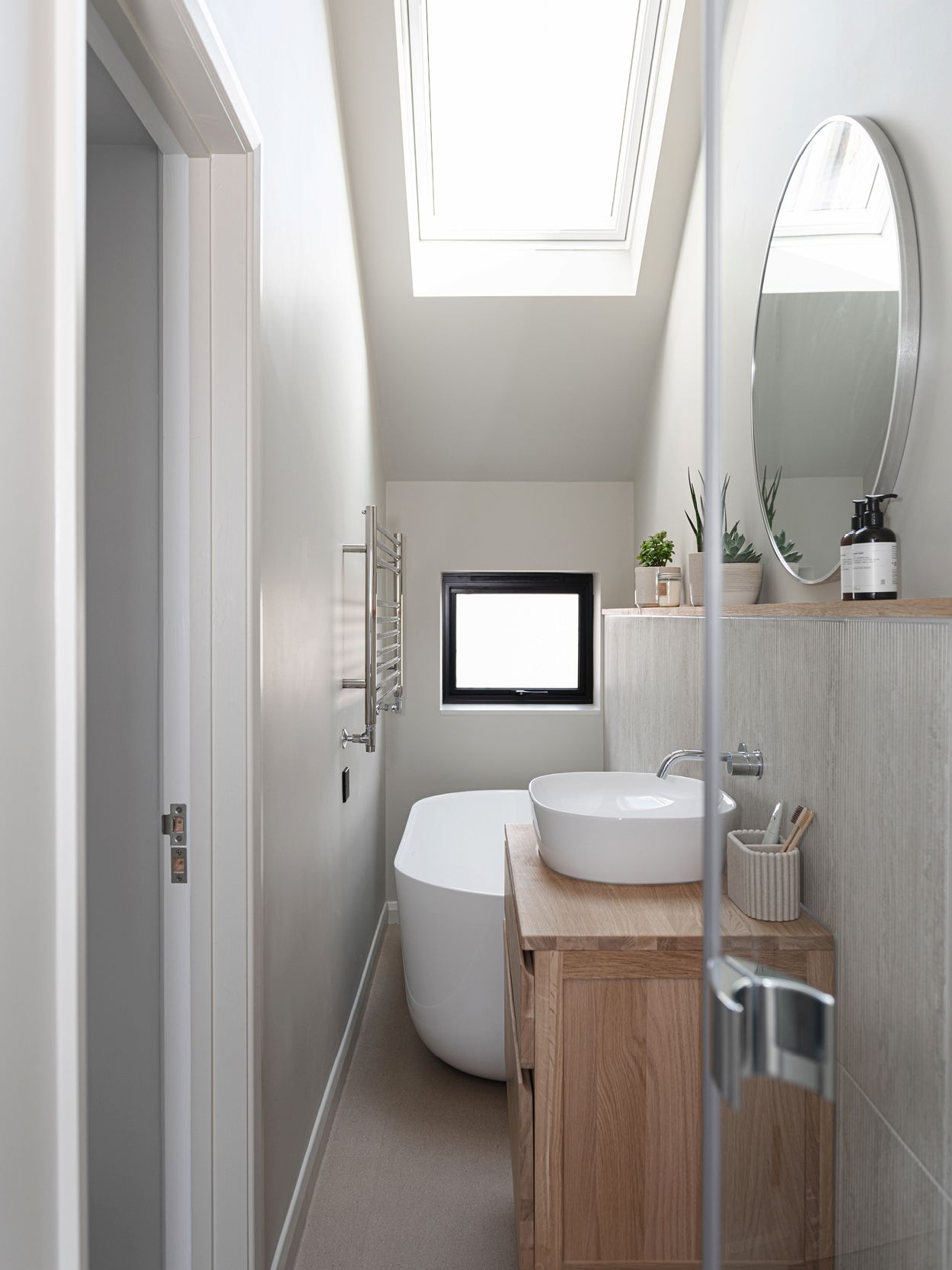 A narrow bathroom with a roof light and a standing bath