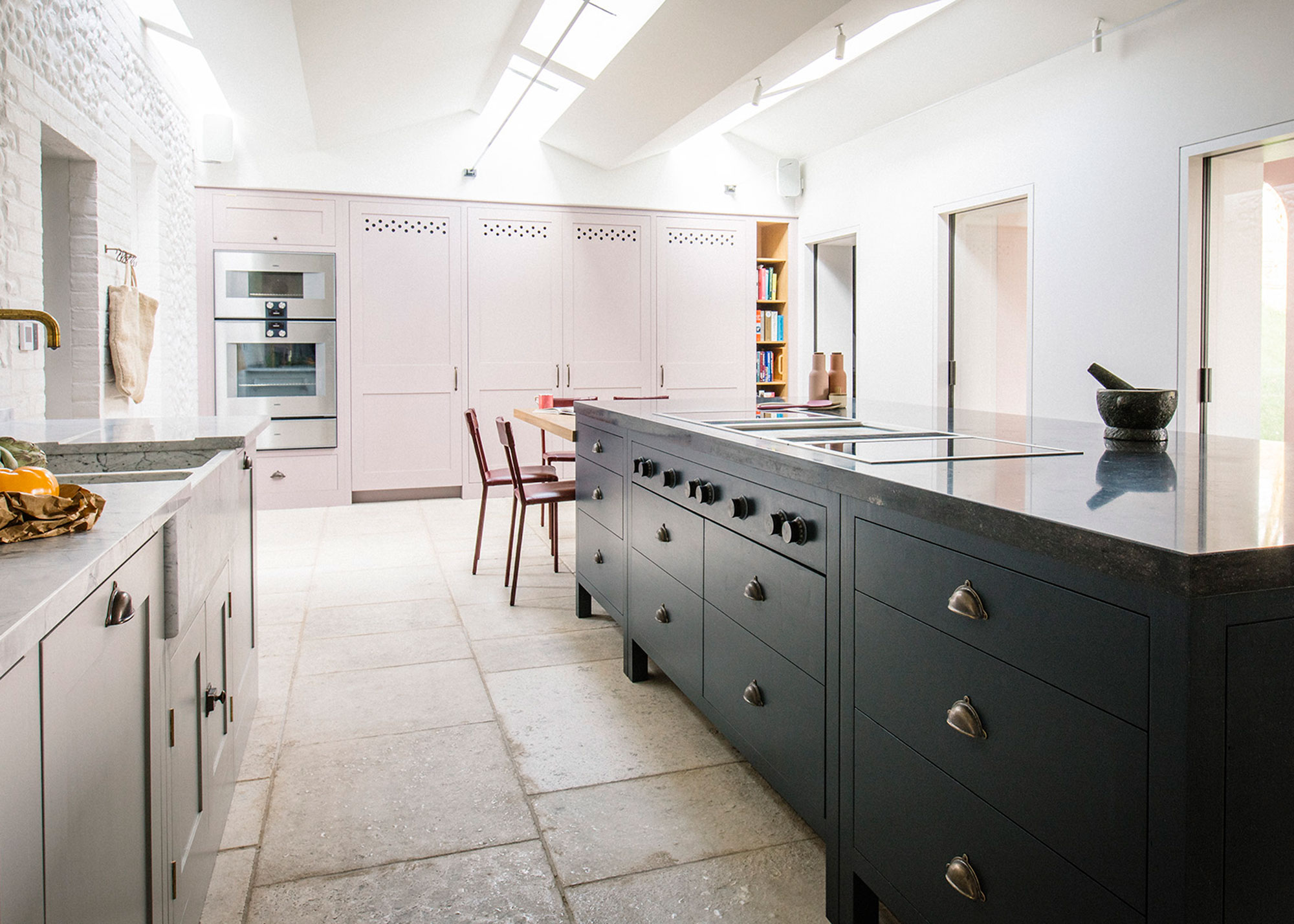 modern black kitchen with drawers and built-in hob with large format stone flooring and pink units