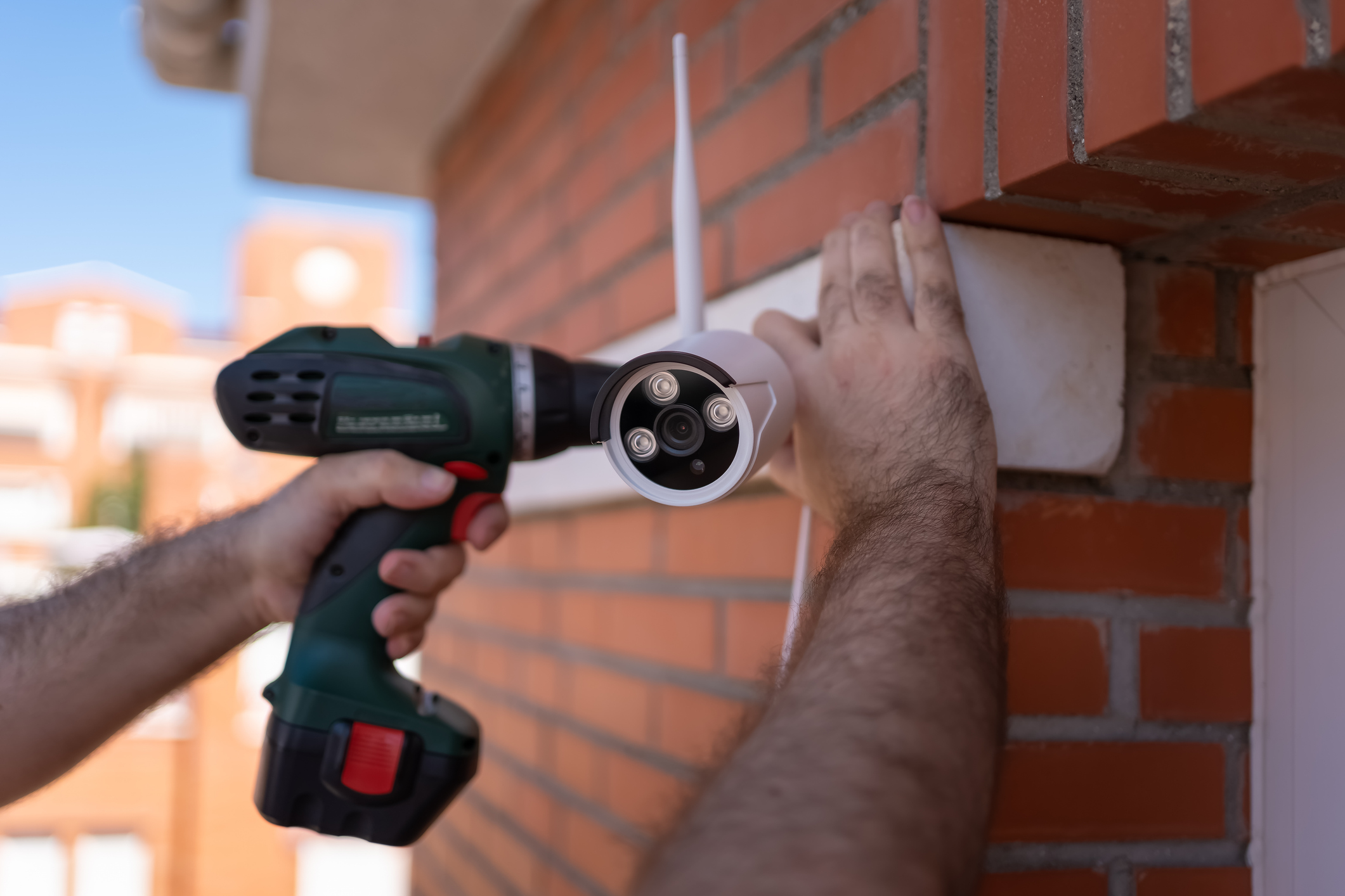 A man installs a security camera on the brick exterior of his home.