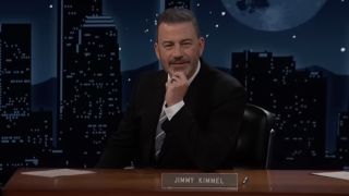 Jimmy Kimmel rubbing his chin behind desk on Jimmy Kimmel Live