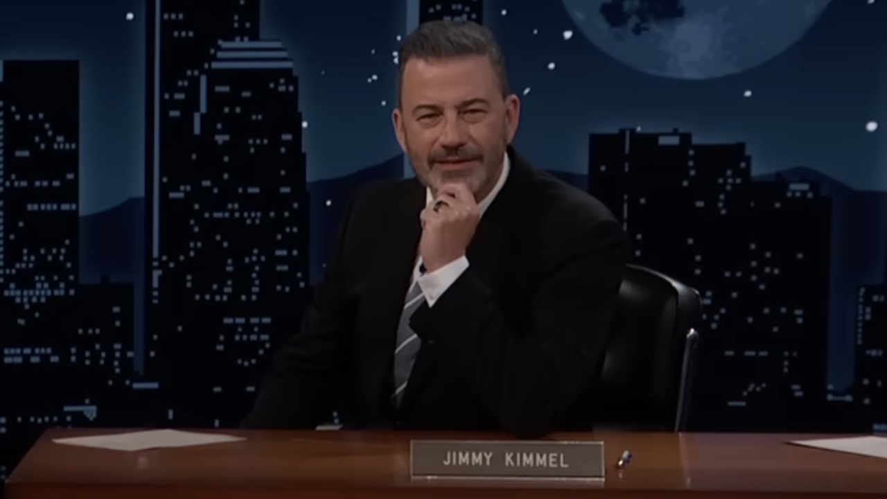 Jimmy Kimmel rubbing his chin behind desk on Jimmy Kimmel Live