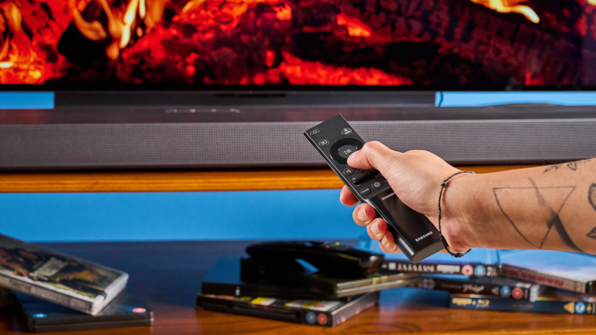the samsung qs750f soundbar with two rear surround speakers and subwoofer photographed against a blue background and a TV