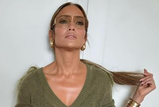 Jennifer Lopez wears a green v-neck sweater, green maxi pleated skirt, brown knee-high moto boots, a Burberry croc-effect handbag, gold earrings, and aviator sunglasses.