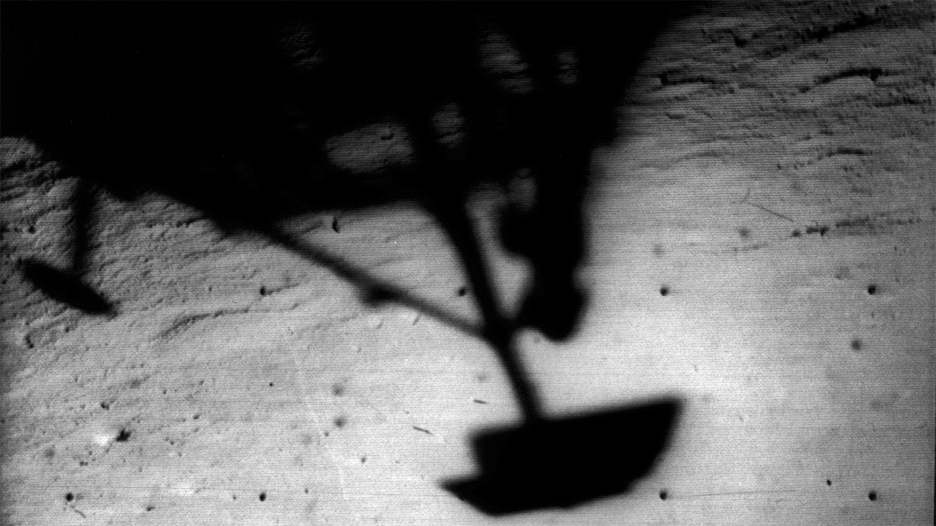 the shadow of a space probe's footpad is seen cast against the surface of a celestial body.