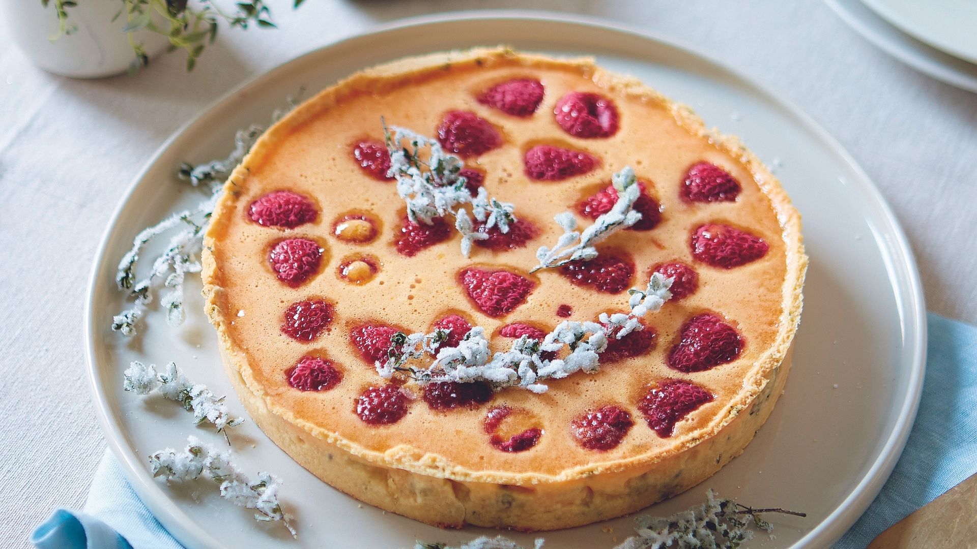 Lemon, Raspberry and Thyme Tart on a large white serving plate beside a blue napkin.