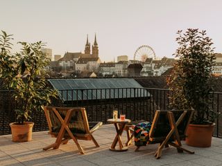 A terrace at the hotel looks out at the skyline of the city. Two wooden lounge chairs with a small table sit in the center.