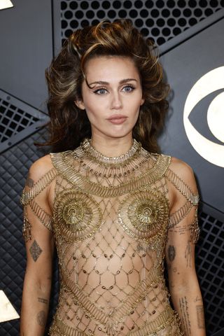 Miley Cyrus wearing a gold metal chain dress with teased hair