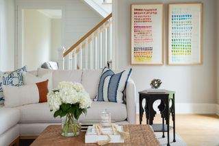 cream sectional with wooden coffee table, black side table, white walls, artwork, view through to staircase, blue stripe cushions