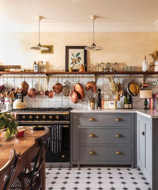 A French country style kitchen with gray cabinets and a brass pot hanger on the wall