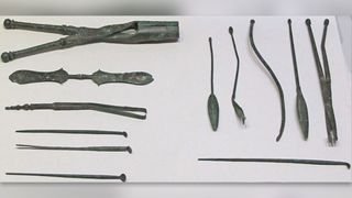 Ancient metal medical instruments displayed on a white background.