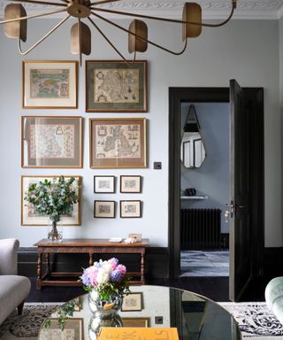 Living room with pale grey walls, white cornice, framed maps, dark grey woodwork and mirrored coffee table.