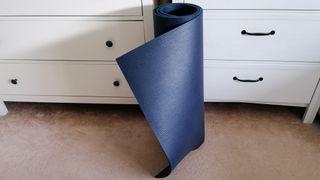 Manduka PROLite yoga mat rolled up and leaning on cupboard