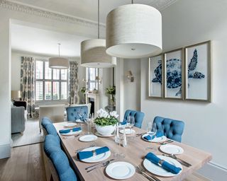 Cream dining room with wood dining table, two cream pendants and blue upholstered chairs