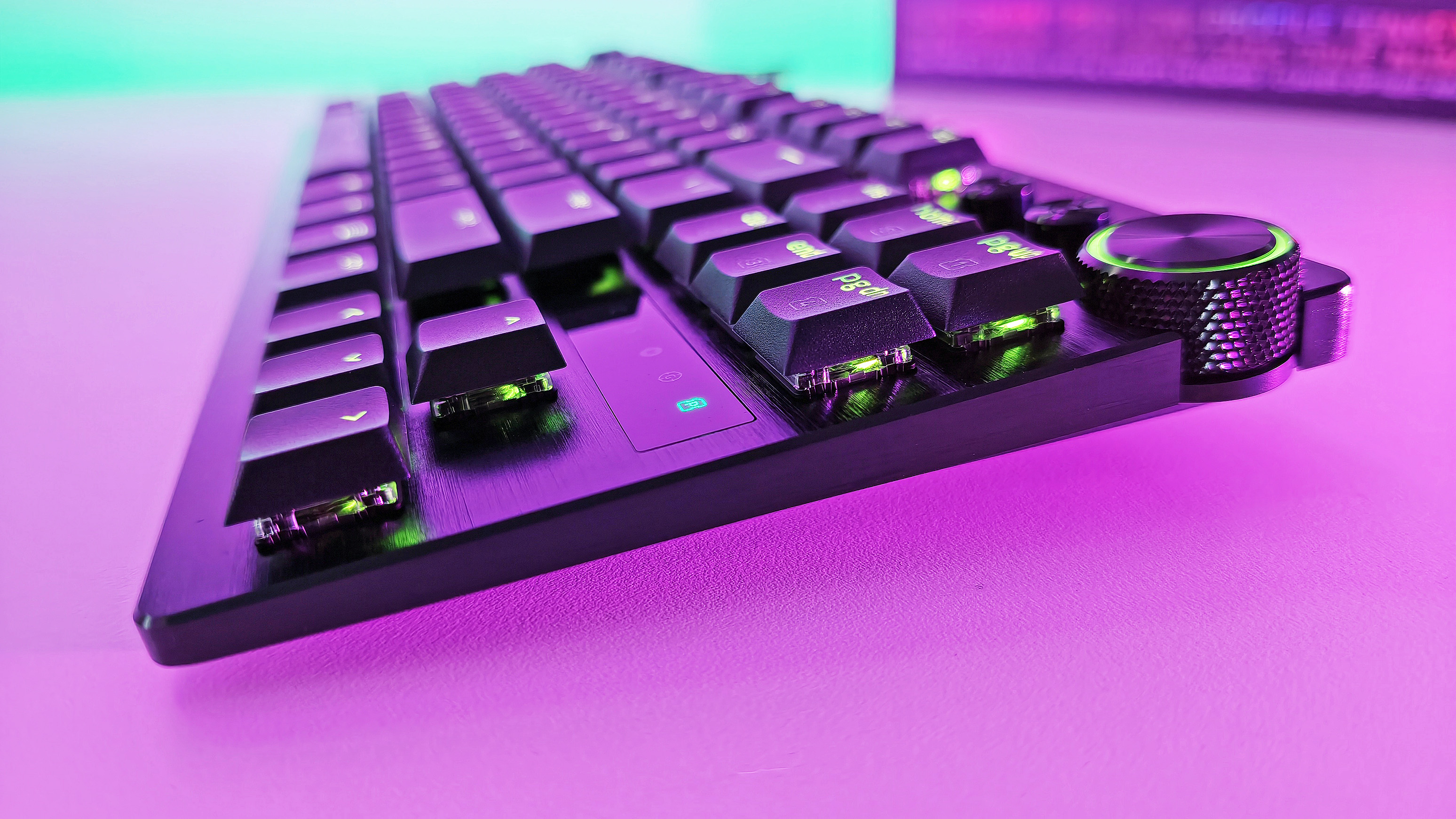 Side-angle view showing the low-profile keycaps, brushed metal plate, and green RGB lighting on the Razer Huntsman V3 Pro TKL keyboard.