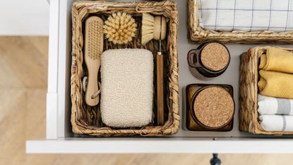 Flat lay view of zero waste products inside organization boxes and wicker baskets. Open drawer at kitchen closet with washing dishes items, bamboo brushes, eco friendly sponge and textile towel