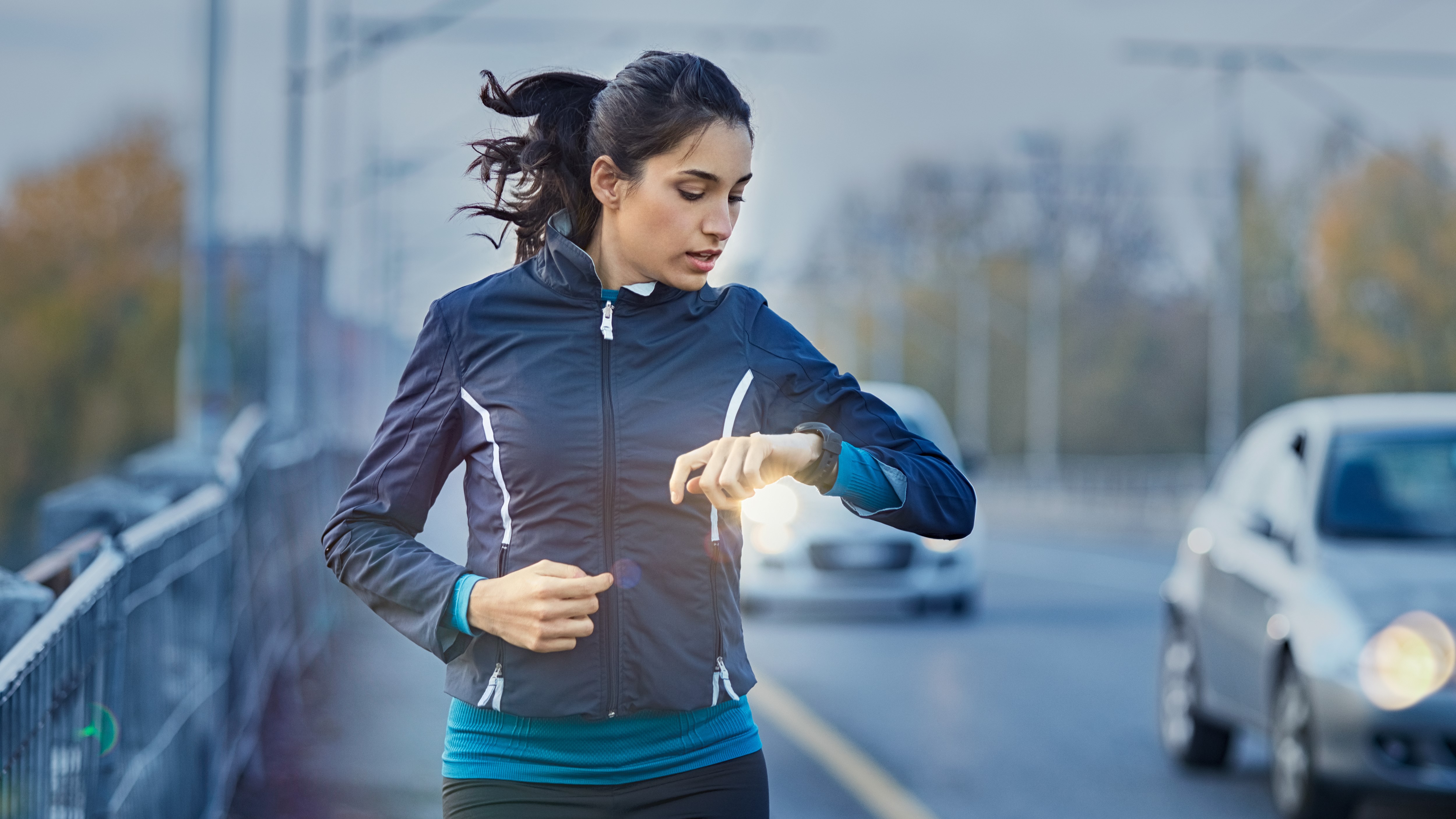 Woman running by a road in the evening, checking her running watch