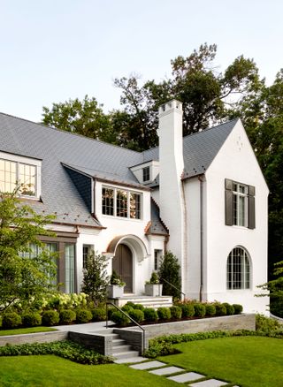large white rendered house with arched front door and landscaped path and mature trees around