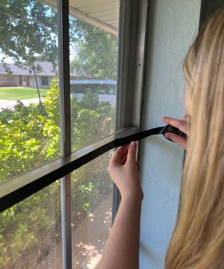 Carefully securing black electrical tape to window frame