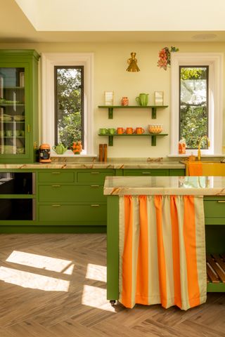 green and orange kitchen with yellow walls, orange accents, curtain in kitchen island, herringbone floor, marble style countertop, open shelving, cabinet on countertop
