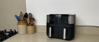 En svart airfryer av typen Ultenic K20 står på en ljus köksbänk bredvid två bestickbehållare.