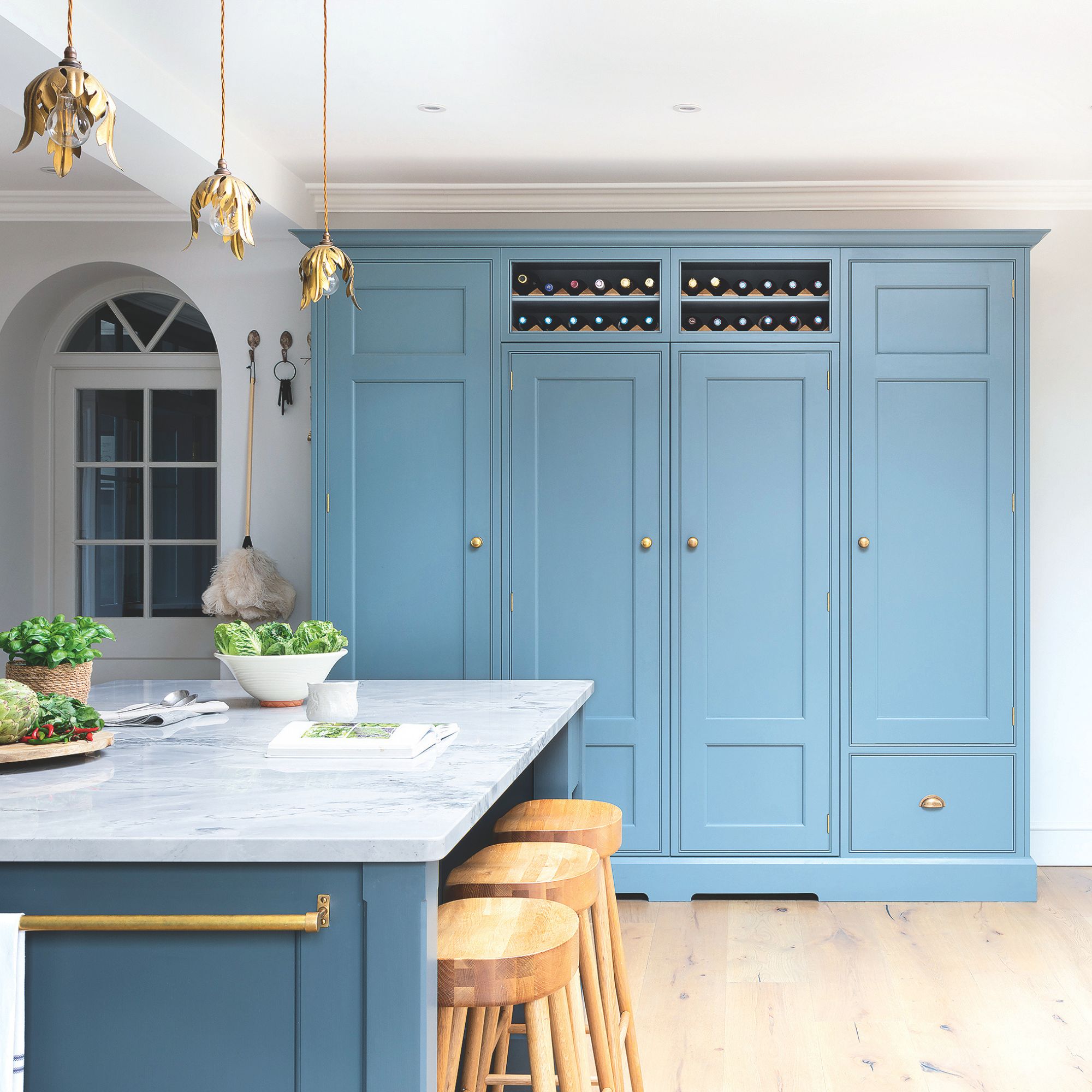 White painted kitchen with large blue cabinets on the back wall and a marble kitchen island with wooden stools