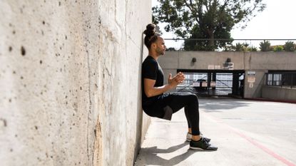 A man performing a wall-sit exercise while training outside