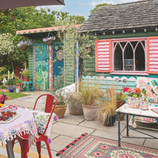 A vibrant boho patio with colourful rugs, potted planted and brightly painted outbuilding.