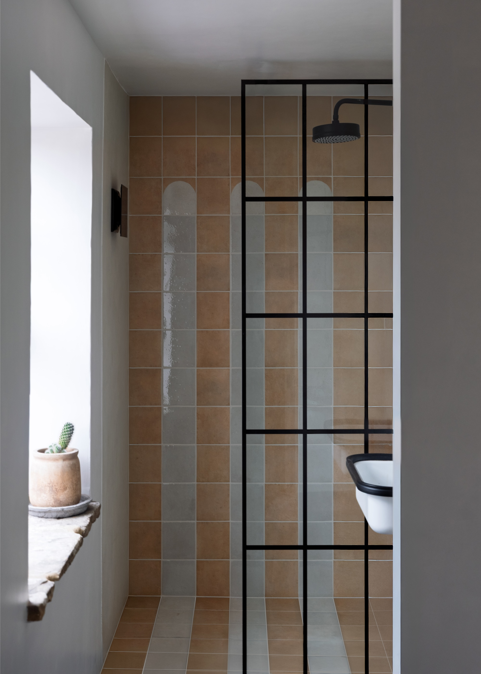 A walk-in shower with a three-stripe among the tiles that starts a portion down the wall and carries on over the floor tiles with a black-framed glass door panel
