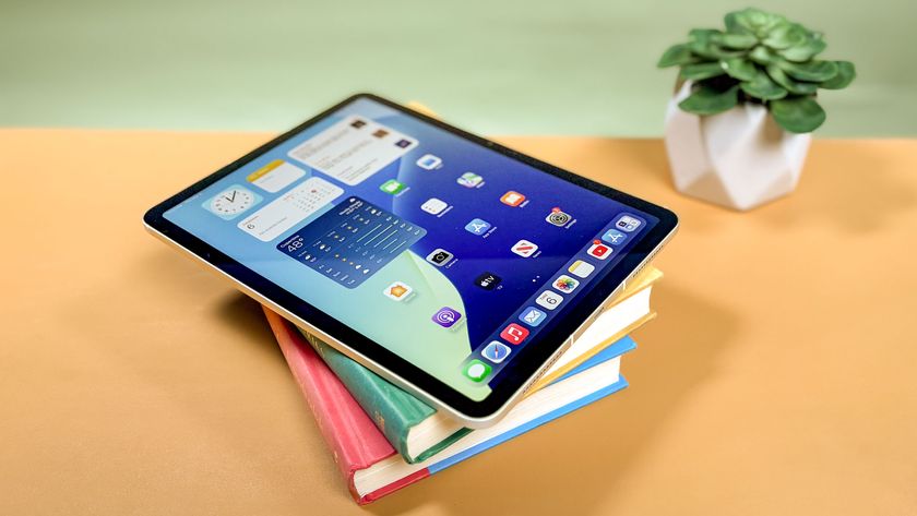 iPad Air M3 on top of a pile of books stacked at an angle on a yellow office table next to a houseplant
